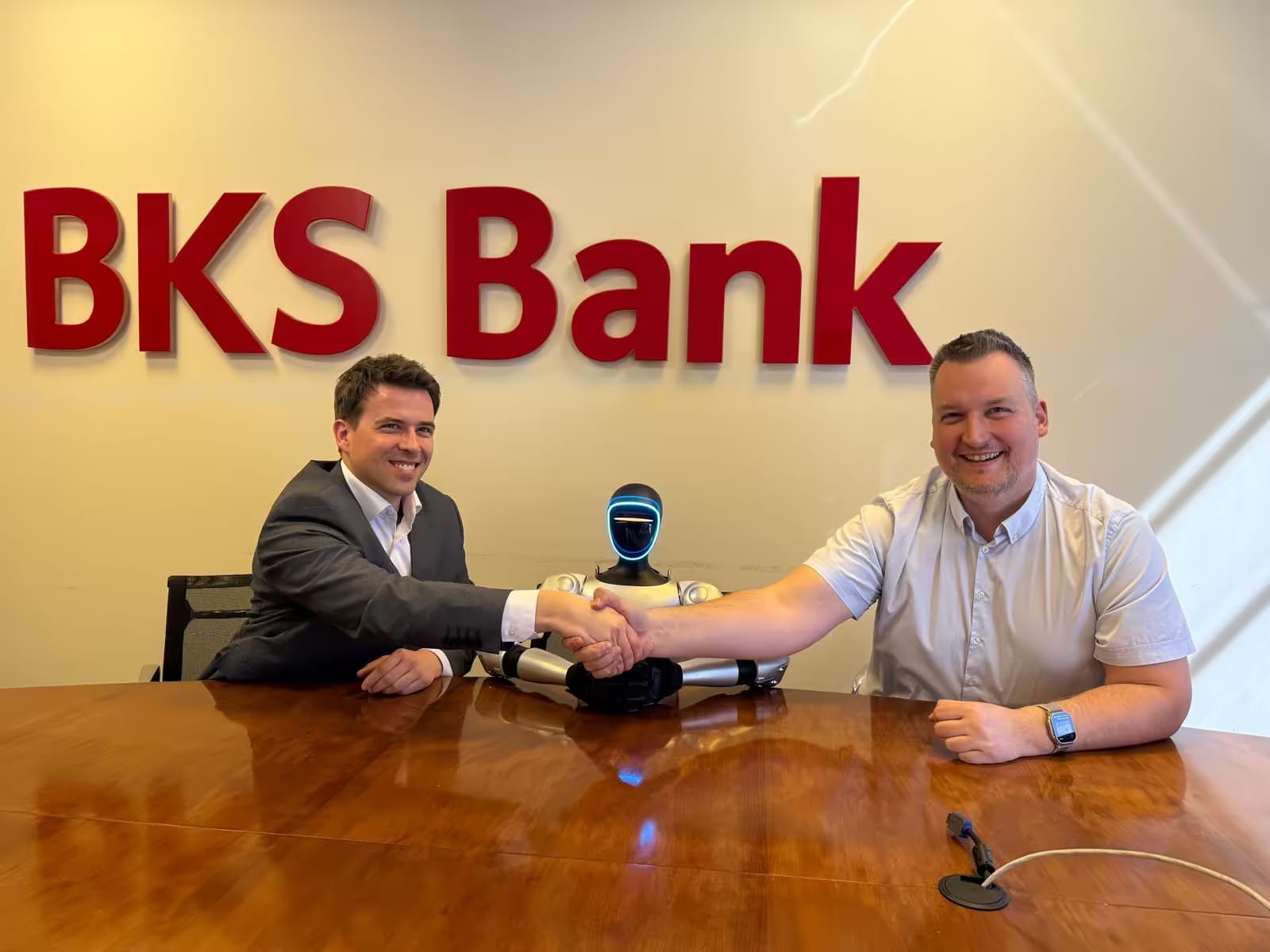 Руковање при склапању сарадње у просторима BKS Bank, између саговорника седи хуманоидни робот.