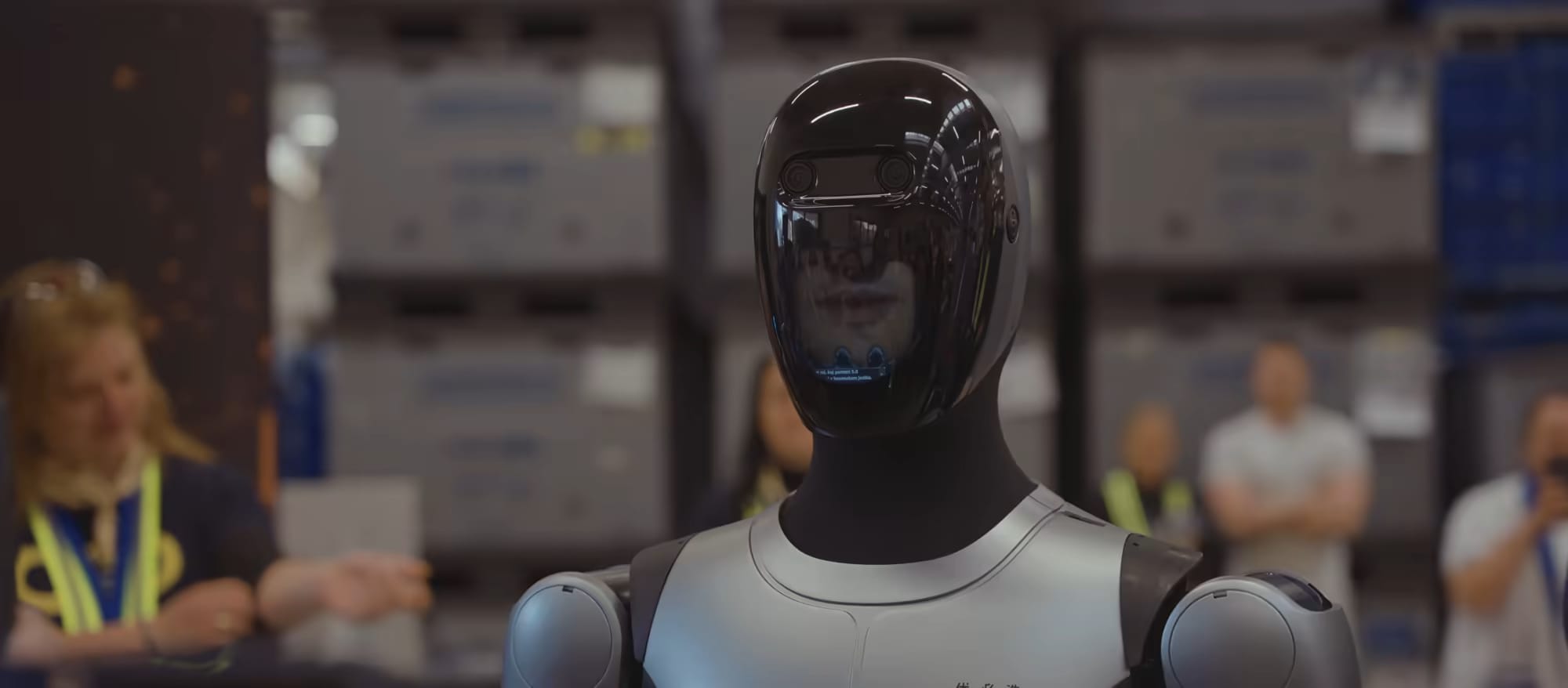 Der humanoide Roboter MAX geht zwischen Arbeitern durch eine Produktionshalle.