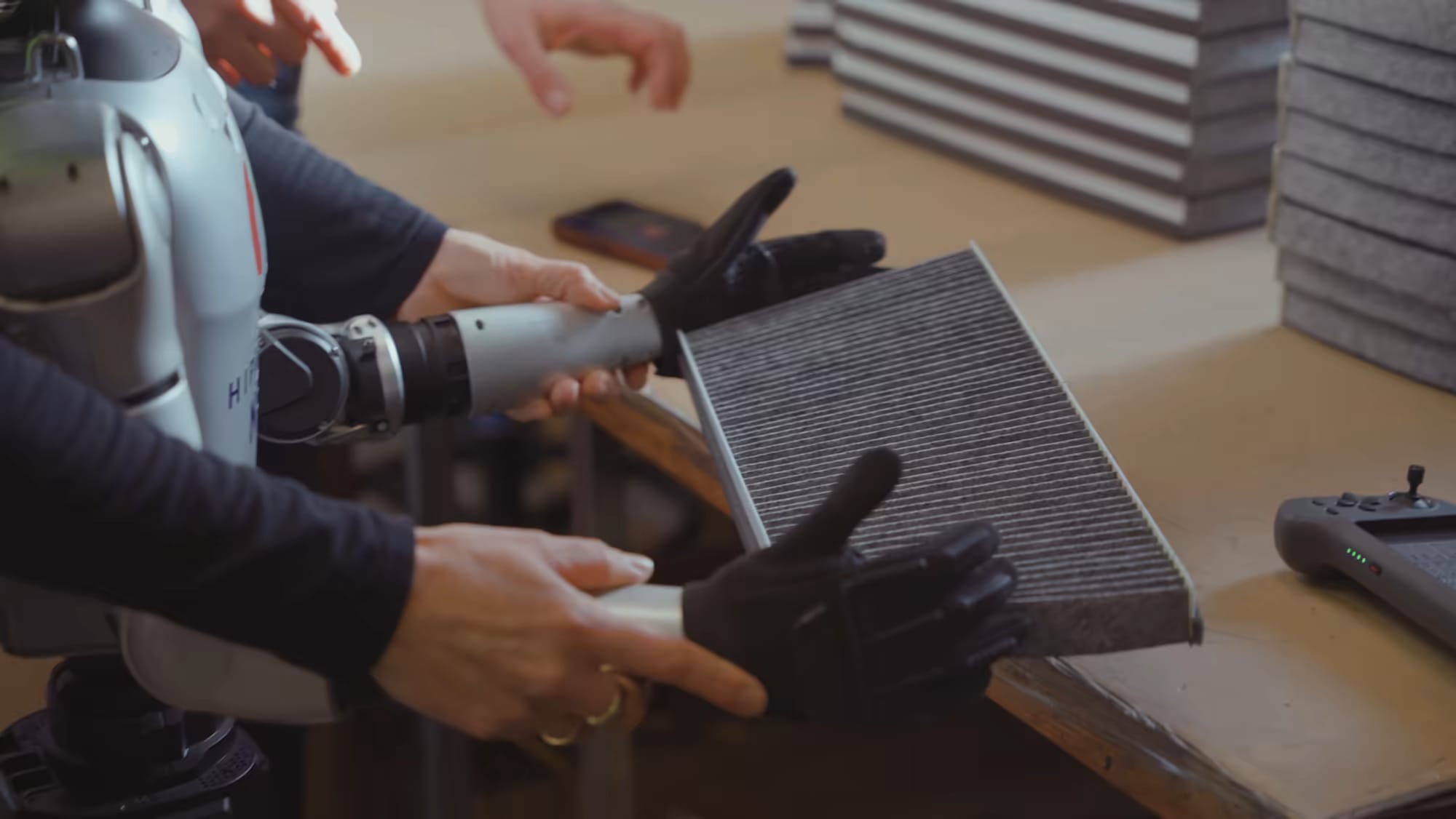 Eine Roboterhand und menschliche Hände halten gemeinsam einen Filter auf der Werkbank.