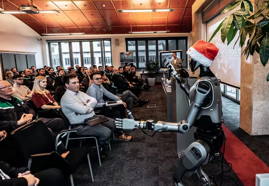 Humanoidni robot z božičkovo kapo pred občinstvom na prednovoletnem srečanju v podjetju