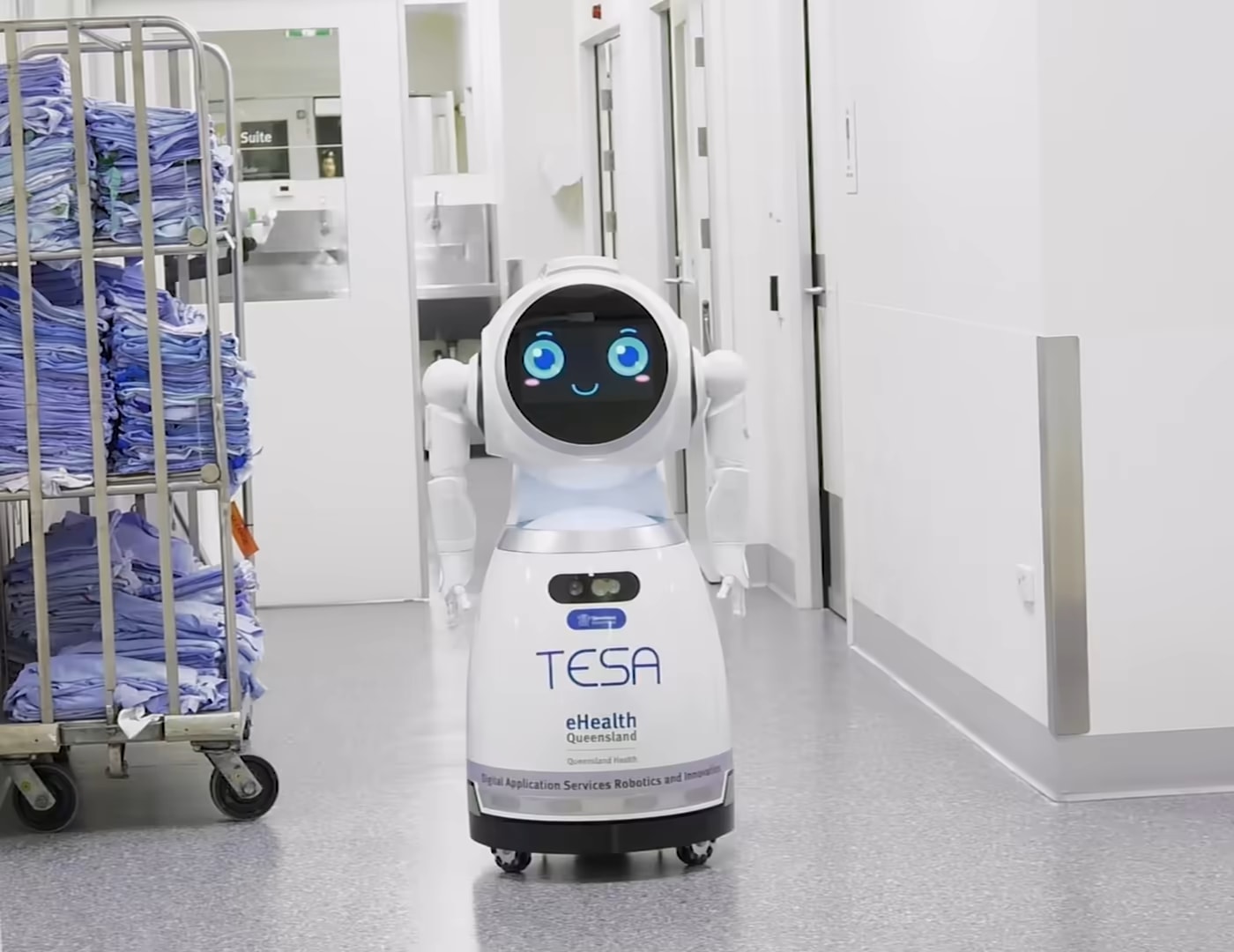Un robot CRUZR en un pasillo de hospital con un carro de ropa de cama detrás.