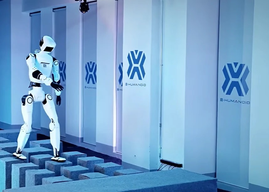 Roboter OMNI tritt über einzeln stehende Blöcke unterschiedlicher Höhe in einer Halle mit X-HUMANOID-Logos an den Wänden