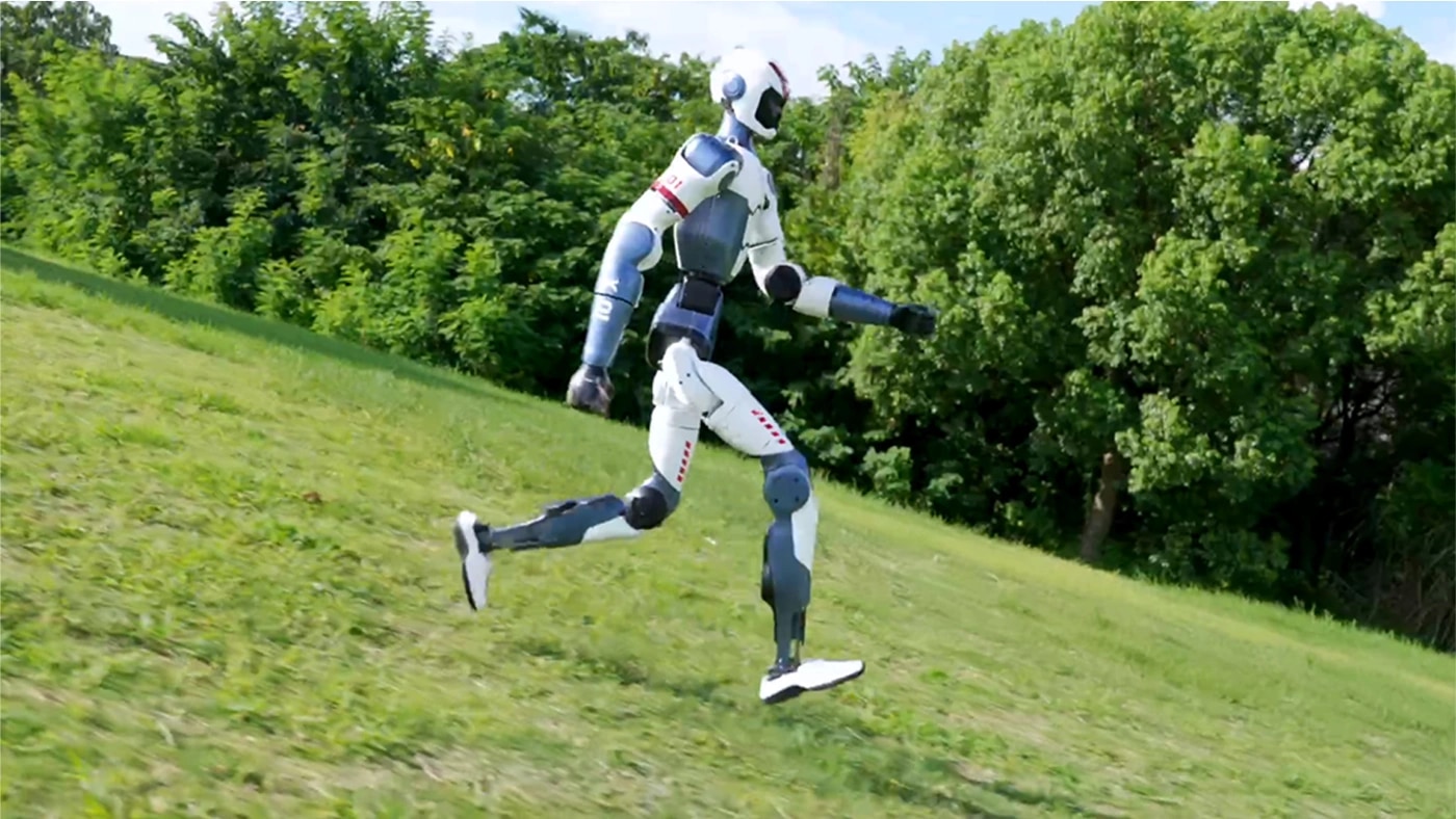 Der Roboter R1 läuft einen grasbewachsenen Hang hinab
