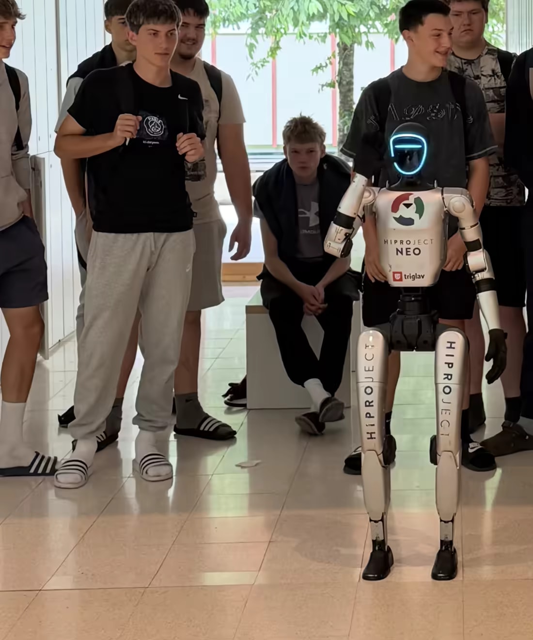 Robot NEO stoji med skupino dijakov na šolskem hodniku
