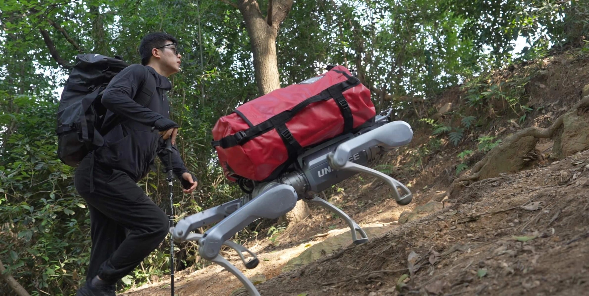 Robot As2 nosi rdečo torbo po gozdni poti ob pohodniku